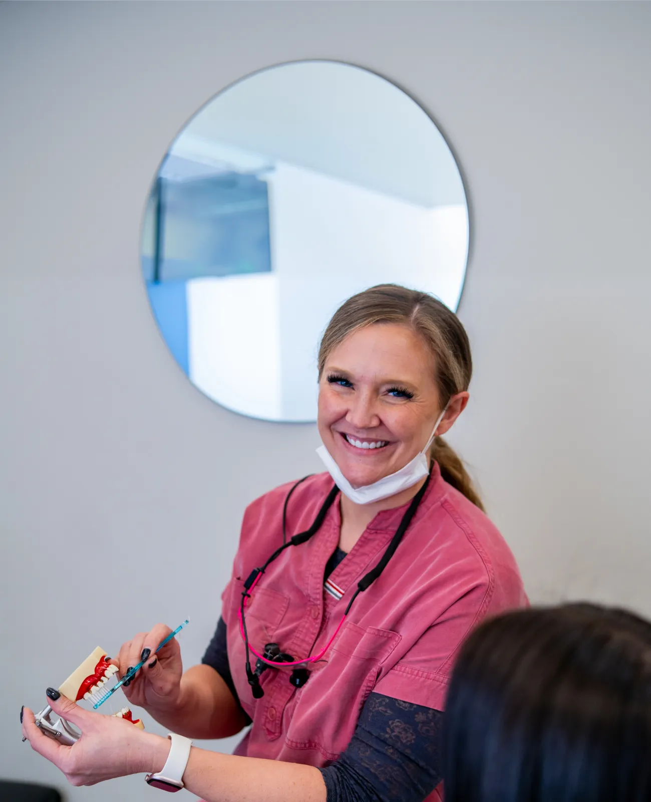 Smiling dental professional demonstrating dental care on a teeth model with a toothbrush.