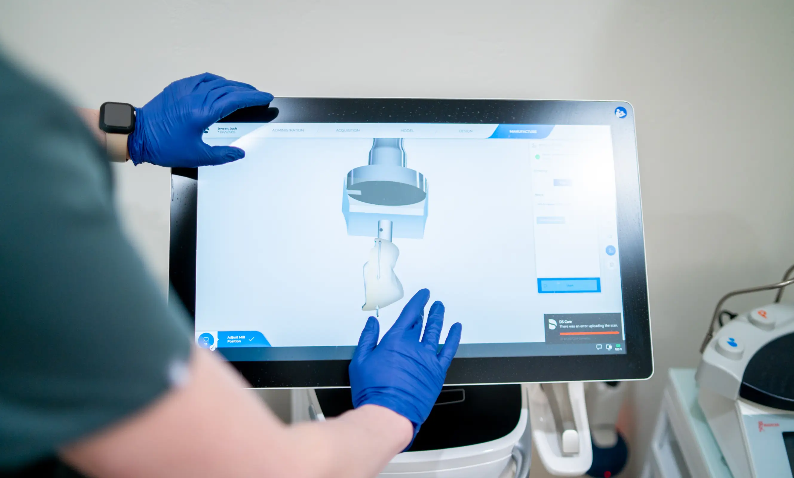 Person with blue gloves using a touchscreen showing a 3D model and milling machine interface.