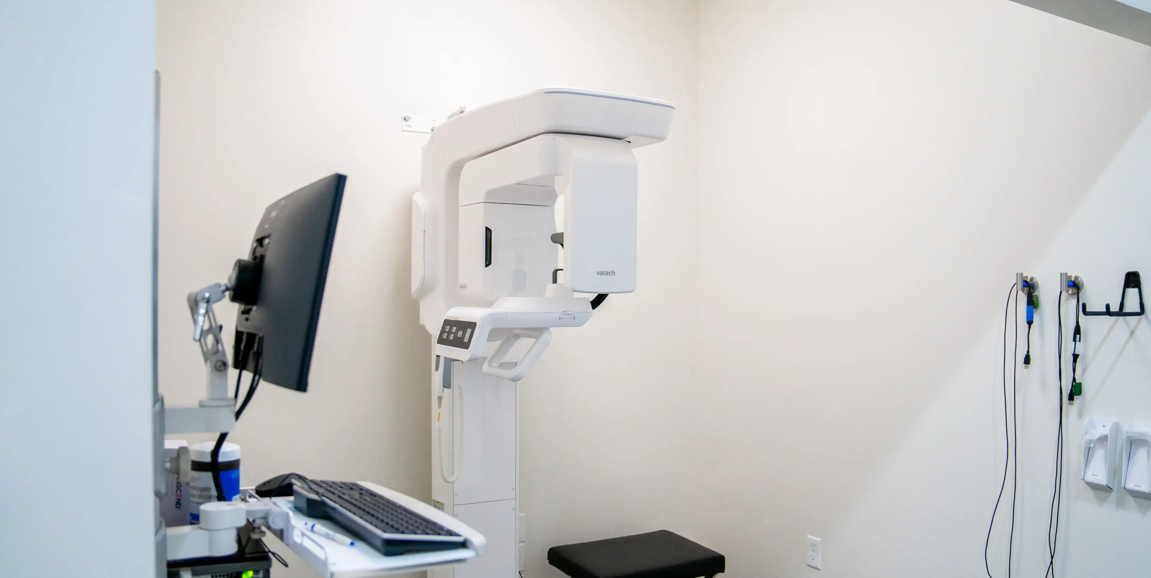 Dental X-ray machine setup with monitor, keyboard, and accessories mounted in a clinical room.