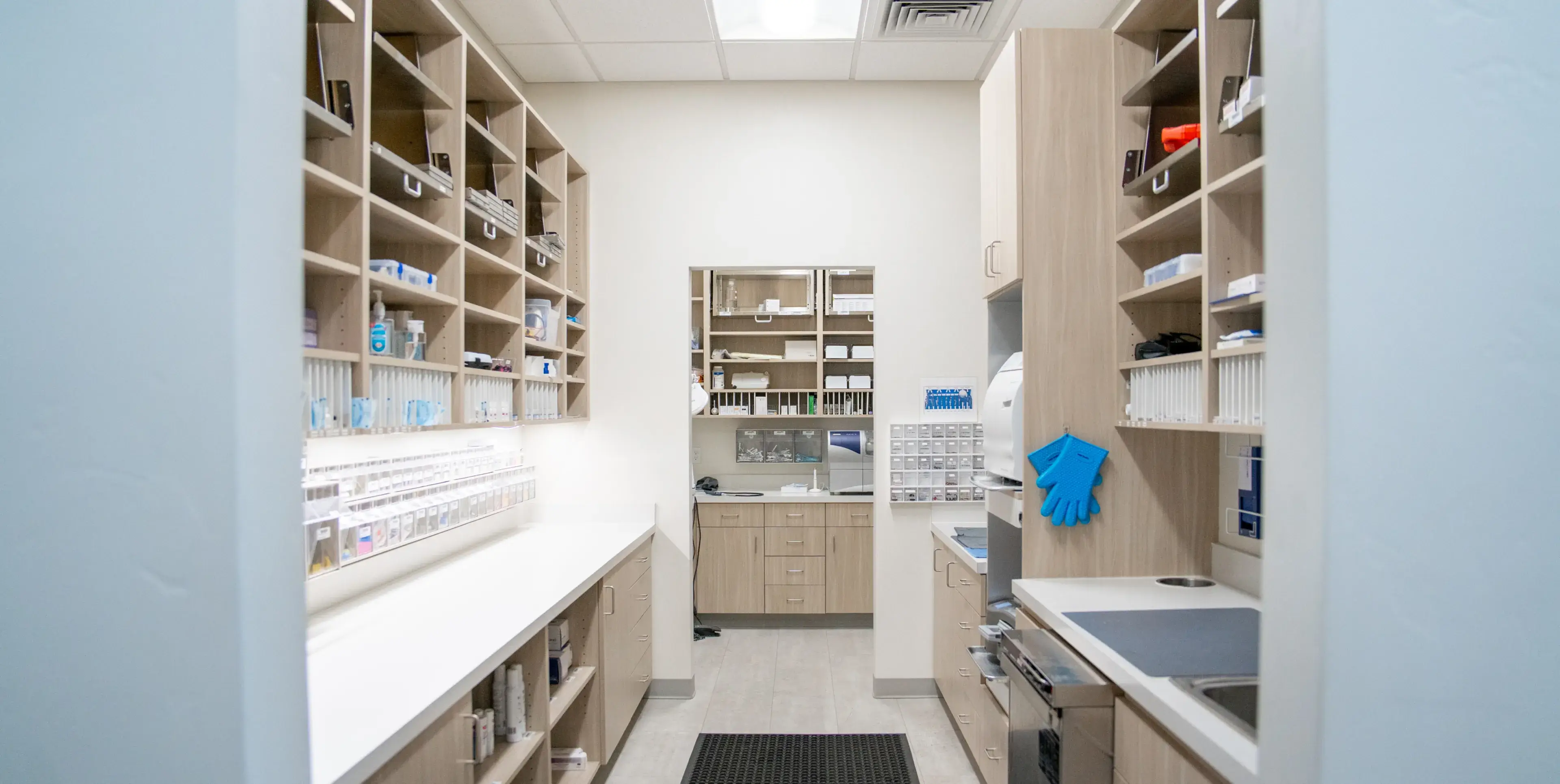 Clean medical storage room with wooden shelves, white countertops, and organized supplies including gloves and sanitizers.